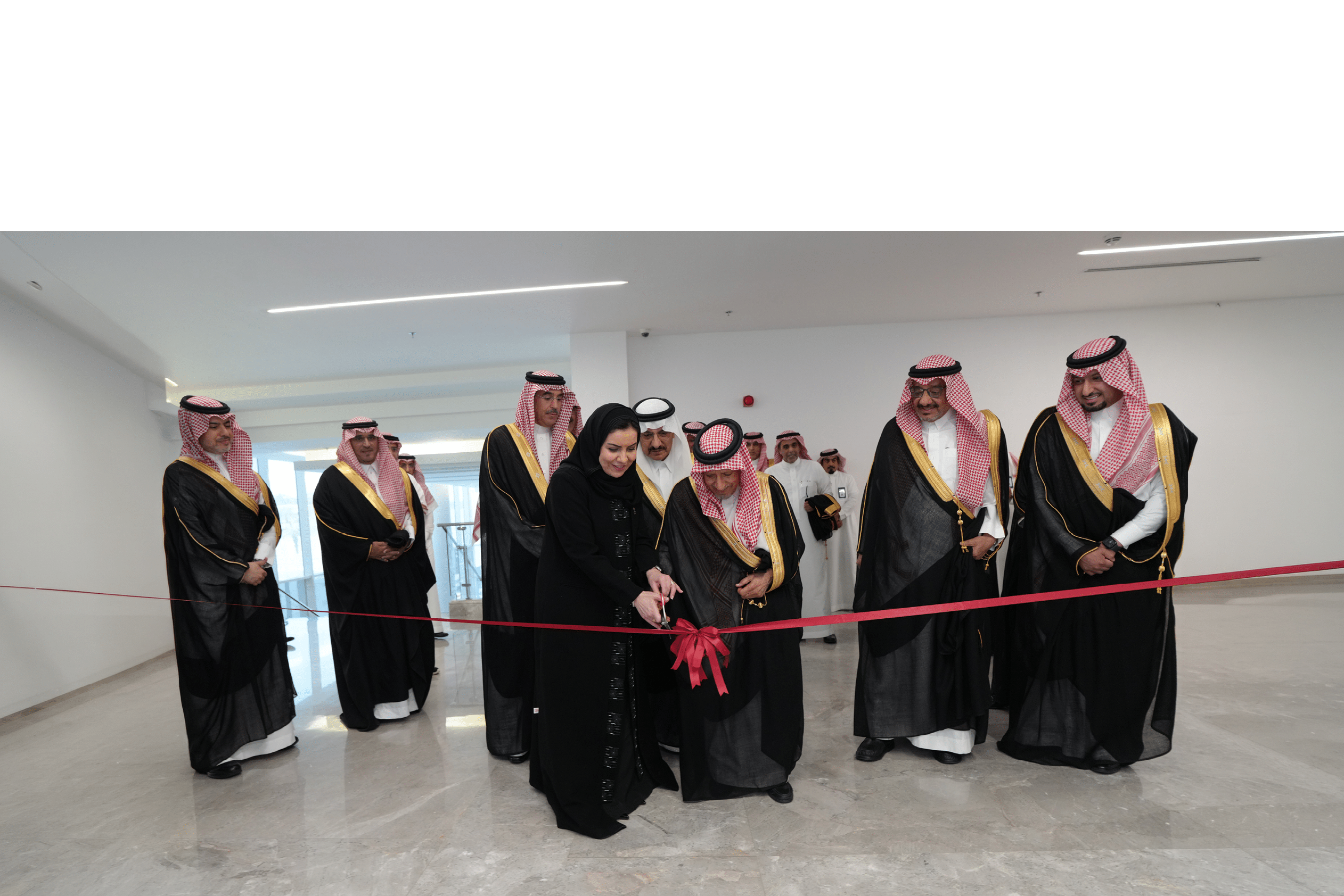 مجموعة من الأشخاص يرتدون ملابس تقليدية رسمية ويشاركون في مراسم قص شريط افتتاح داخل مبنى حديث. Description generated by AI