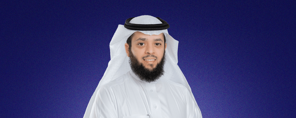 شخص يرتدي ثوبًا وغطاء رأس تقليديين ويبتسم أمام خلفية زرقاء داكنة. Description generated by AI