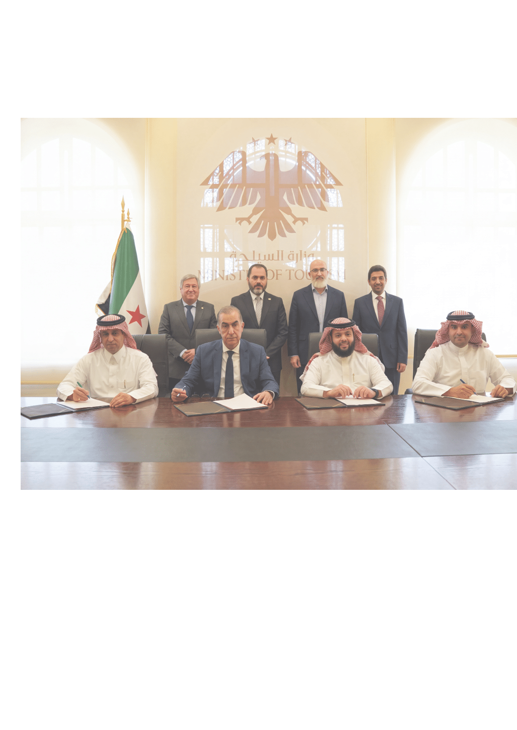 مجموعة من الأشخاص يرتدون ملابس رسمية وتقليدية يجلسون ويوقعون مستندات في غرفة اجتماعات تحمل شعار وزارة السياحة. Description generated by AI