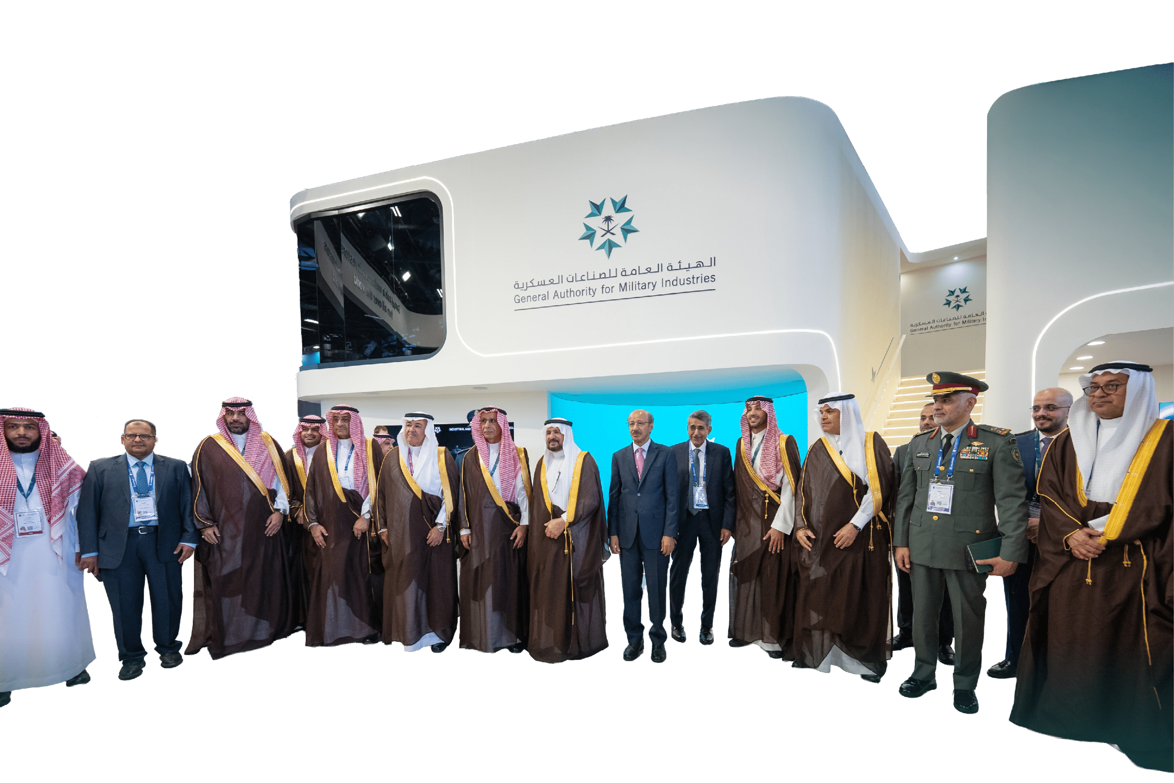مجموعة من الأشخاص يرتدون ملابس تقليدية رسمية وبدلات يقفون أمام جناح يحمل شعار الهيئة العامة للصناعات العسكرية في معرض أو مؤتمر. Description generated by AI