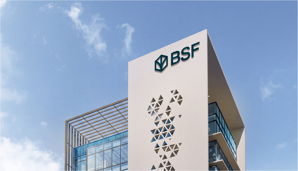 مبنى حديث ذو تصميم معماري مميز يحمل شعار BSF على واجهته البيضاء مقابل سماء زرقاء صافية. Description generated by AI