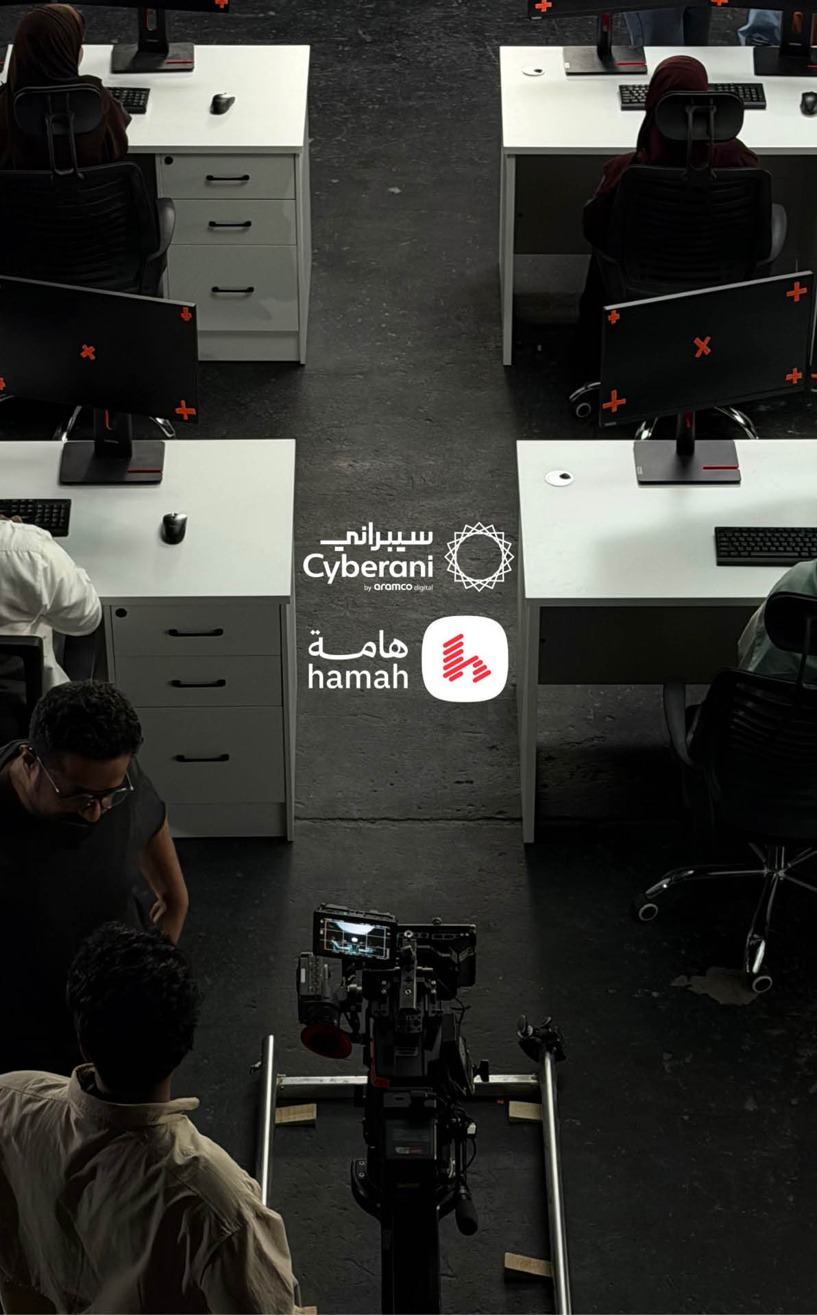 عدد من الأشخاص يجلسون أمام شاشات كمبيوتر في مكتب مظلم بينما يراقب شخصان آخران كاميرا تصوير على عربة في الوسط. Description generated by AI